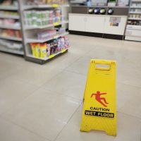 Yellow sign showing warning of caution wet floor. Wet floor sign is in the supermarket against the background of blurry products standing on the shelves. Selective focus.